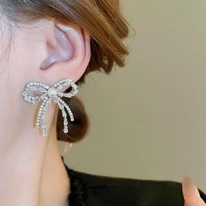 Close-up of bow knot tassel earring with rhinestones and pearl on model's ear