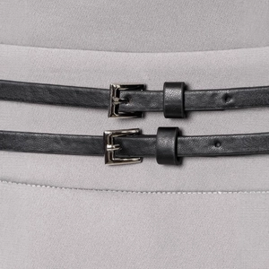 Close-up of dual black leather belts with silver metal buckles on gray pleated dress