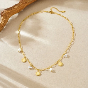 Collier chaîne trombone dorée avec pendentifs coquillages et perles blanches sur fond beige