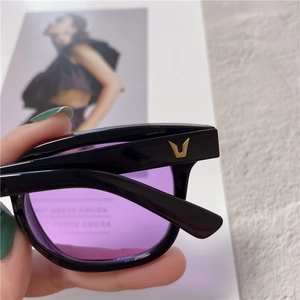 Macro detail of purple lenses and black square frame featuring iconic metallic V-shaped logo