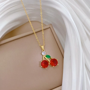 Elegant gold cherry pendant necklace with red crystals on a beige luxury display box