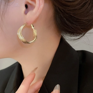 Detail shot of a model wearing a twisted gold geometric hoop earring with metallic gloss