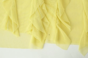 Detailed macro view of yellow mesh fabric with layered ruffle design on the long dress