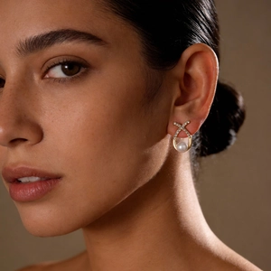 Close-up of golden crossover earrings with white pearl and sparkling rhinestones on model
