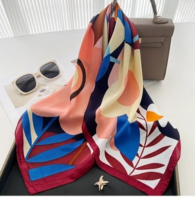 Detailed view of silk square scarf with bold abstract floral print on a leather bag