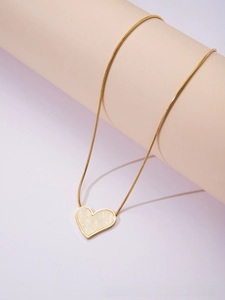 Detailed shot of golden heart pendant necklace with cream enamel on pink display stand