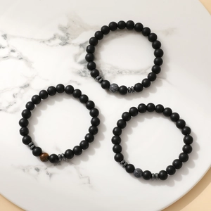 Three men's 8mm natural stone bracelets with matte black beads and tiger eye on marble tray