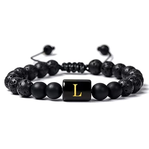 Détail macro du bracelet en pierre de lave avec perle dorée gravée de la lettre L