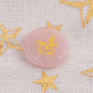 Detailed view of pink rose quartz disc with gold skull engraving on white linen fabric