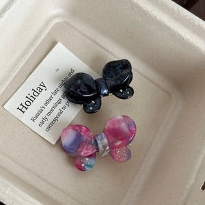 Bow-shaped marble acetate hair clips with crystal accents on a minimalist tray