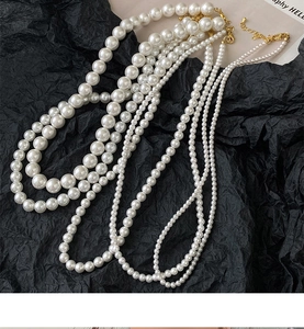 Vue détaillée de colliers de perles blanches superposés avec fermoir doré sur fond noir