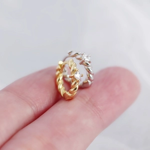 Detailed macro of twisted metal huggie earrings with square zircon on fingertips