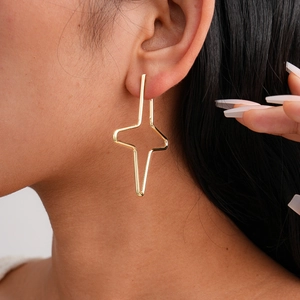 Close-up of minimalist gold cross star earring on model ear with fine metal lines
