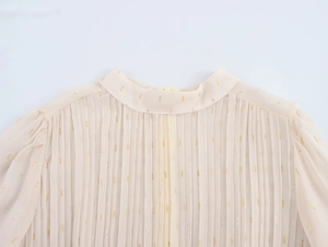 Detail of elegant beige chiffon dress featuring fine pleats and golden metallic dots