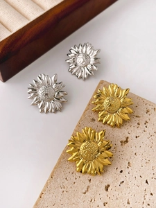 Macro detail of sunflower stud earrings in gold and silver finish on textured stone