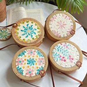 Handcrafted round rattan shoulder bag with colorful shell inlay on white table
