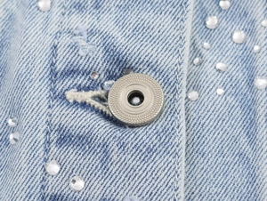 Détail du tissu denim bleu clair avec bouton métallique et ornements en strass brillants