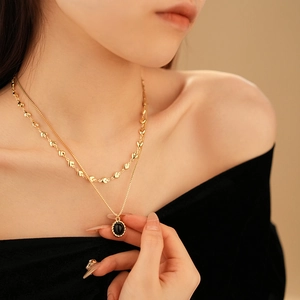 Detail of a layered gold necklace with black oval pendant and small heart accents