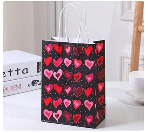 Detail of a black gift bag with red and pink hearts and twisted white paper handles