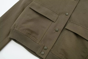 Detail of olive green bomber jacket featuring heavy canvas texture and metal snap buttons