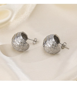 Gros plan de boucles d'oreilles argentées à texture irrégulière sur fond de soie beige