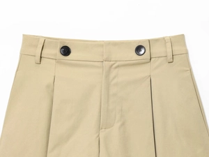 Dettaglio dei pantaloni in twill kaki con doppi bottoni neri e design della vita a pieghe