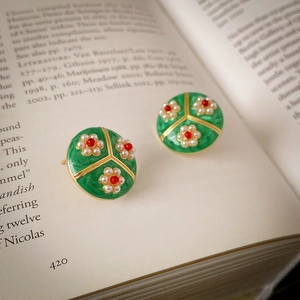 Vintage gold-plated floral earrings with green enamel and white pearls on an open book