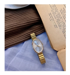 Detail of vintage oval gold-tone watch featuring a silver sunburst dial and chain strap