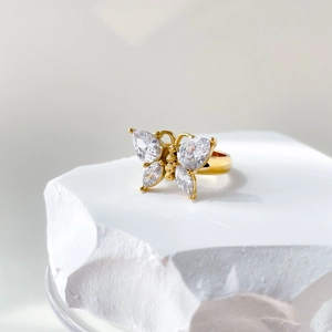 Détail d'une bague papillon dorée ornée de zircons marquise sur un socle blanc