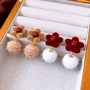 Detail of floral velvet stud earrings with soft pom-pom pendants in brown and red colors