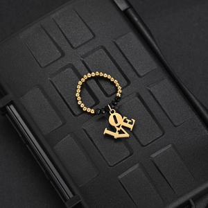 Detail shot of a beaded elastic ring with a gold 'LOVE' pendant on a textured background