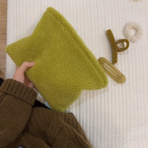 Green plush fleece cosmetic bag held by hand, soft fuzzy textured winter pouch for women