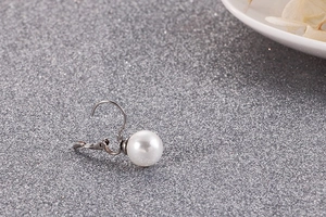 Gros plan détaillé d'une boucle d'oreille perle blanche et crochet argenté sur fond gris