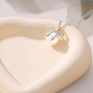 Detailed macro of a S925 sterling silver bow and pearl necklace on a beige heart tray