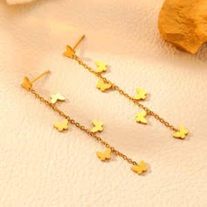 Elegant gold stainless steel butterfly tassel earrings displayed on a textured beige surface