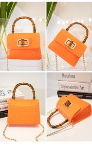 Detail view of orange crocodile pattern mini bag featuring a bamboo handle and metal chain