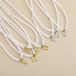 Elegant gold and silver letter pendant pearl necklaces on a beige textured background