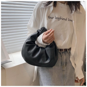Detail of black pleated cloud handbag featuring a soft knotted handle and matte texture