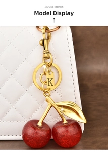 Detail of red cherry keychain with gold letter K tag hanging on a white quilted bag