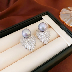 Macro shot of silver pearl earrings with zircon fan-shaped leaf design on satin