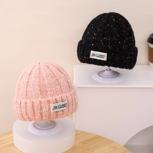 Close-up of knit beanie hats with colorful speckles and smiling face patch details