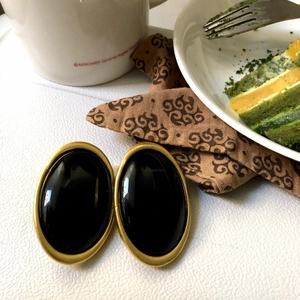 Vintage oval black stud earrings with gold border displayed on a cozy tea time background