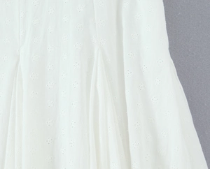 Dettaglio del tessuto in pizzo bianco con ricami floreali traforati e texture eleganti