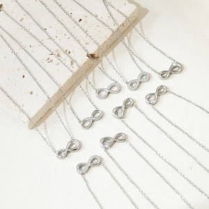 Silver infinity heart necklaces with cubic zirconia on a minimalist stone background