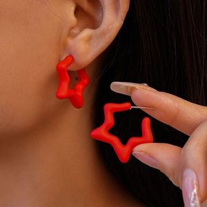 Close-up of matte red star-shaped acrylic hoop earrings worn by a model for a chic look