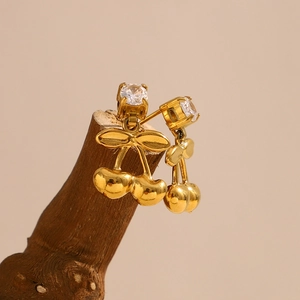 Détail de boucles d'oreilles cerises dorées 18K avec zircons sur un support en bois