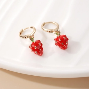 Creative red strawberry drop earrings with gold hoops on a white textured plate