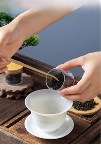 Detail of hand using wood spoon to scoop tea from heat resistant glass jar