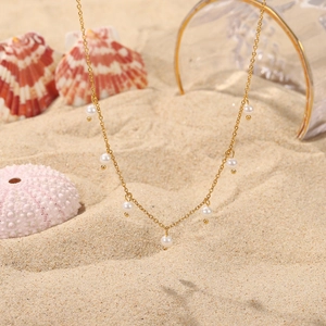 Detail of 18K gold stainless steel necklace with white pearls on a beach setting