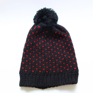 Detailansicht der schwarzen Strickmütze mit roten Herzen und großem flauschigem Pompon